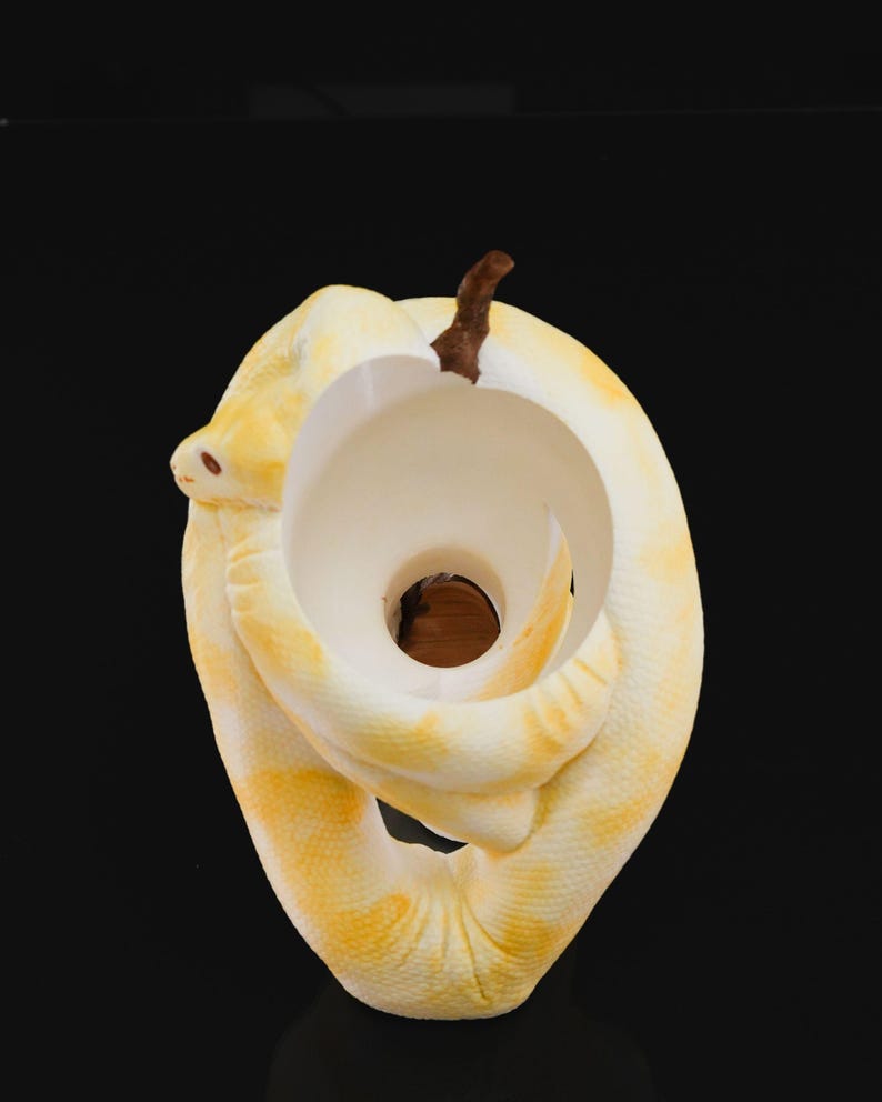 May include: A decorative sculpture of a coiled snake in shades of yellow and white, with a brown stem-like element at the top. The snake's body forms a circular shape with a central opening, creating a unique and artistic design.