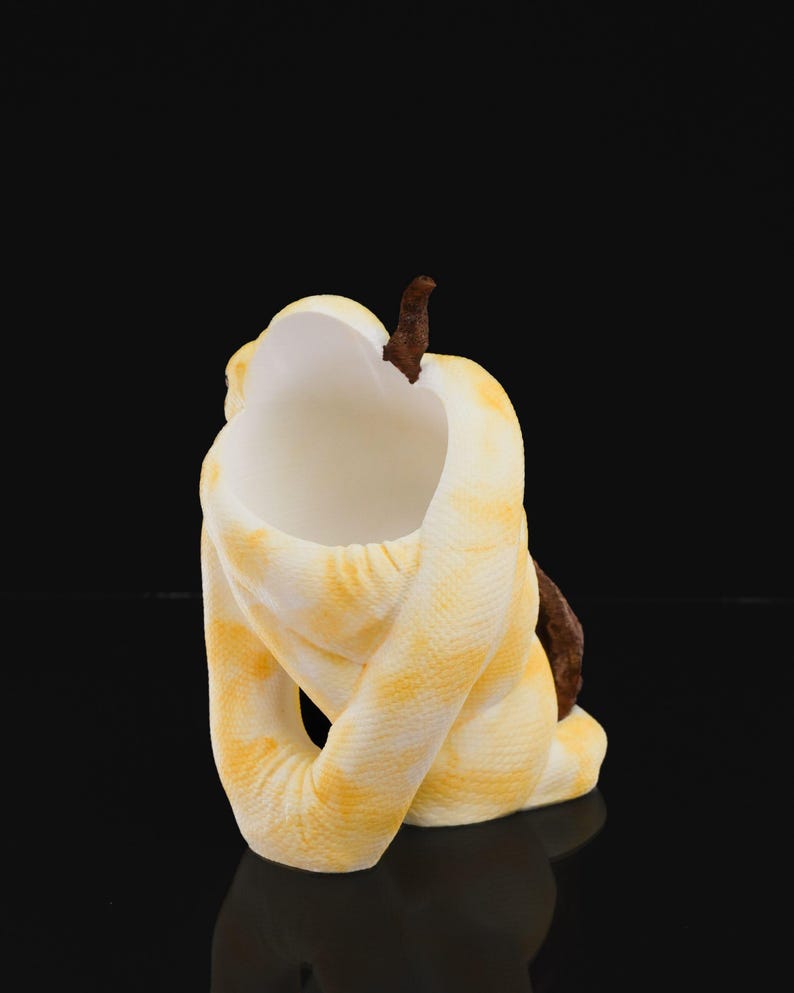 May include: A ceramic sculpture of a coiled snake in yellow and white with a brown accent. The snake's body is wrapped around itself, creating a unique and artistic form. The sculpture is set against a black background.