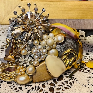 May include: A heart-shaped piece of jewelry made from various vintage brooches, pearls, and rhinestones. The piece is gold and silver toned and features a bird, a flower, and a key.