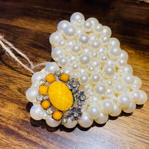 May include: A heart-shaped ornament made of white pearls with a yellow and silver decorative accent in the center.