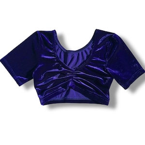 May include: A short-sleeved, deep purple velvet top. The top features a gathered detail at the bust and a scoop neckline. The fabric has a soft, lustrous appearance. The garment is designed for comfort and style.