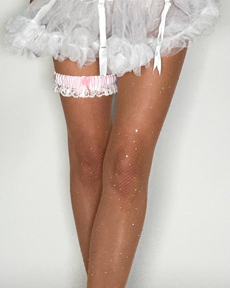 May include: White lace garter with a pink satin bow. The garter is worn on a leg with sheer, sparkly tights.