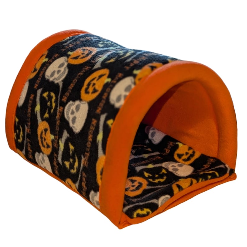 Może przedstawiać: Tunel dla zwierząt domowych o tematyce Halloween w kolorze pomarańczowym i czarnym. Tunel ma czarną tkaninę z pomarańczowymi dyniami i białymi czaszkami. Krawędzie są wykończone w jasnym pomarańczu. Na tkaninie wydrukowano napis "Happy Halloween".