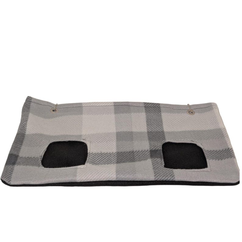 May include: A gray and white plaid pet bed with two black openings. The bed is rectangular and has a soft, plush appearance. Metal grommets are visible at the top corners.