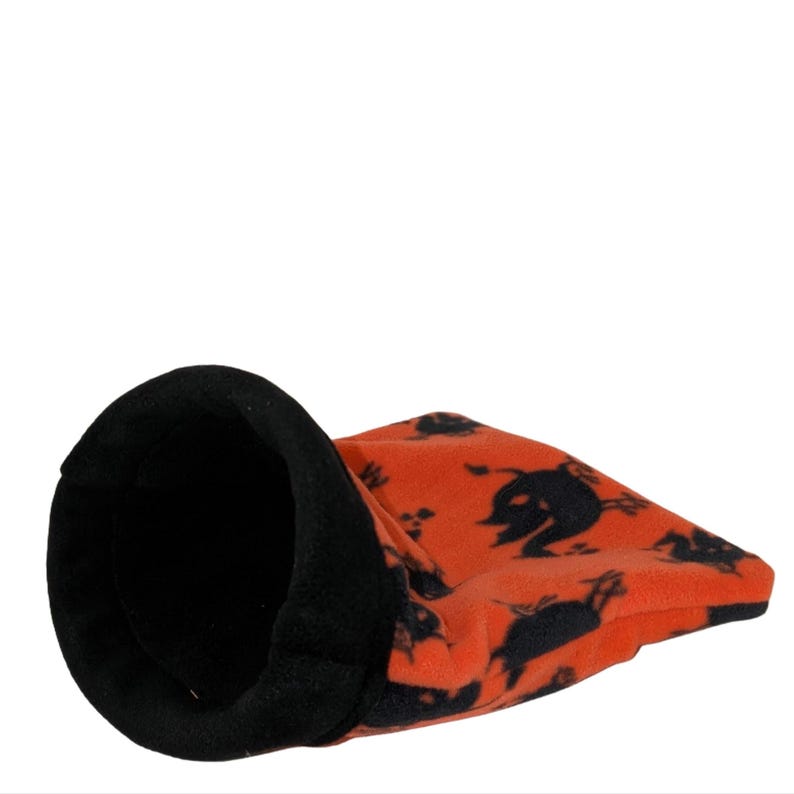 May include: An orange and black pet bed with a tunnel design. The bed is made of soft fleece material and features a black interior and a pattern of black silhouettes. The tunnel shape provides a cozy space for small pets.