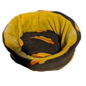 May include: A round pet bed with a plush design. The bed features a dark brown interior with orange accents and a yellow exterior. The bed is designed for small pets and is made of soft, comfortable material.