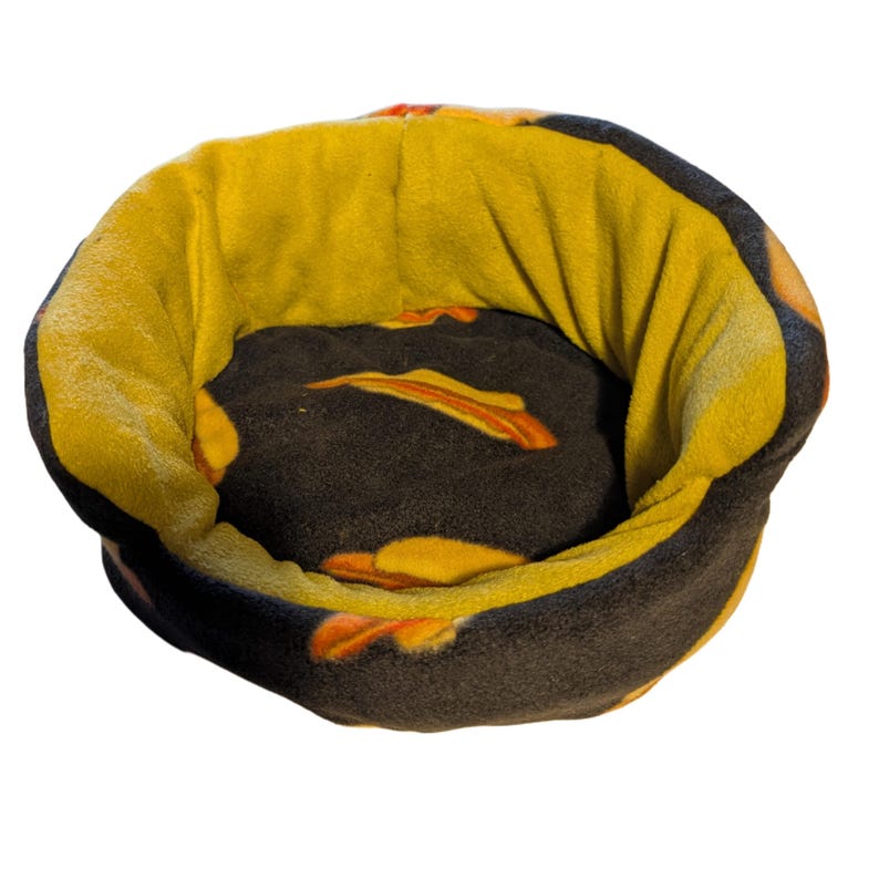 May include: A round pet bed with a plush design. The bed features a dark brown interior with orange accents and a yellow exterior. The bed is designed for small pets and is made of soft, comfortable material.