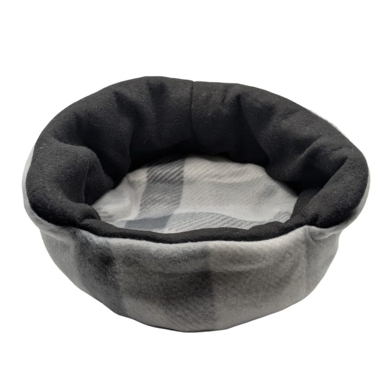 May include: A gray and black pet bed with a plaid interior. The bed has a soft, plush exterior in shades of gray and a black rim. The interior features a gray and white plaid pattern, providing a cozy space for small pets.