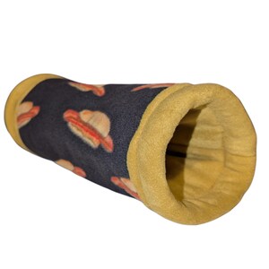 May include: A cylindrical pet tunnel with a navy blue exterior patterned with hot dogs. The interior and the tunnel's openings are a golden yellow color. The tunnel is made of soft fabric.