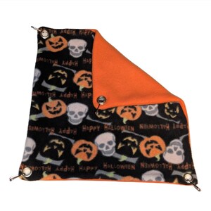 Może przedstawiać: Akcesorium dla zwierząt domowych o tematyce Halloween. Czarna tkanina przedstawia pomarańczowe dynie, białe czaszki i słowa "Happy Halloween". Druga strona jest w jednolitym pomarańczowym kolorze. Metalowe przelotki znajdują się w każdym rogu.