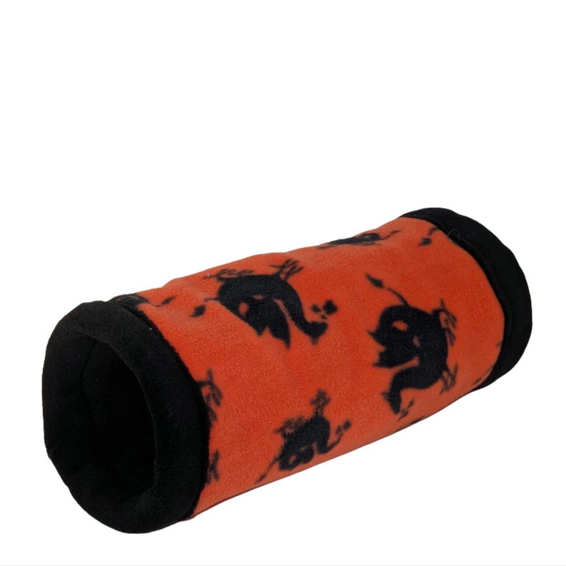 May include: An orange fleece pet tunnel with black trim and a repeating black silhouette pattern. The tunnel is cylindrical and appears soft, designed for small animals to play and rest inside.