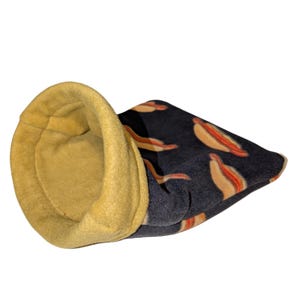 May include: A small pet bed with a yellow interior and a dark blue exterior patterned with hot dogs. The bed is made of soft fleece material and is designed to provide a cozy space for small animals.
