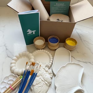 May include: A craft box containing art supplies, including paint, brushes, and white plaster shapes. The box has a sticker that says "This box has good vibes only."