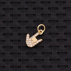 May include: A gold-coloured charm in the shape of a hand making the 'I love you' sign. The charm is encrusted with small, clear crystals. It has a small loop at the top for attaching to a necklace or bracelet.