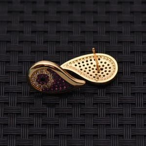 May include: Gold-toned stud earring with a teardrop design. The earring features a section of small, round, purple and white gemstones. The back of the earring has a perforated design and a post for insertion.