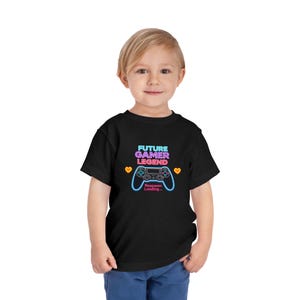 May include: Black toddler t-shirt with a neon-style graphic that reads "FUTURE GAMER LEGEND" above a game controller design. The phrase "Respawn Loading..." is below the controller. Two orange hearts flank the controller.