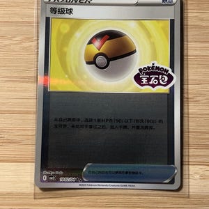 Könnte beinhalten: Eine Pokémon Trainer-Karte mit einem Pokéball-Design in Gelb, Schwarz und Rot. Die Karte enthält japanischen Text und das Pokémon-Logo. Sie befindet sich in einer Schutzhülle.