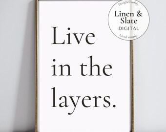 May include: A framed print with the words "Live in the layers" in a bold, black font on a white background. The frame is gold-colored. The print also includes the text "Linen & Slate DIGITAL" and "Designed softly, Lived simply."