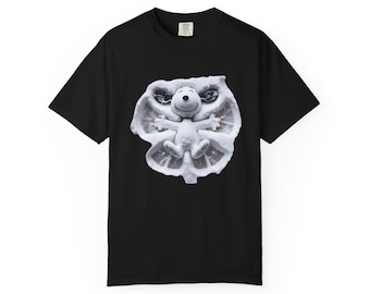 Peut inclure: T-shirt noir avec un motif de Snoopy faisant un ange de neige. L'image montre Snoopy allongé dans la neige, les bras et les jambes écartés. Le motif est en nuances de blanc et de gris, avec Snoopy souriant au centre.
