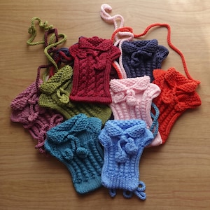 Puede incluir: Una colección de monederos tejidos a mano en varios colores, incluyendo rojo, rosa, azul, verde y morado. Cada monedero presenta un diseño único con un cuello y una correa, mostrando intrincados patrones y texturas de tejido.