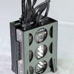 Puede incluir: Una caja de ordenador negra y gris con recortes circulares. La caja tiene un panel lateral de plástico transparente y cables negros que se extienden desde la parte superior. La caja está diseñada para albergar componentes informáticos.