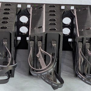 May include: Black computer server rack with three bays, each with a black component and attached cables. The rack has a perforated design and includes silver-colored circular elements.