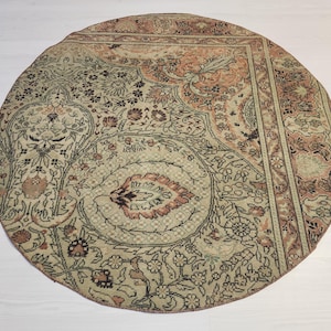 May include: A round area rug featuring a complex, multi-coloured floral and paisley pattern in shades of muted peach, sage green, and dark brown. The design includes intricate botanical motifs, scrolling vines, and a decorative border.