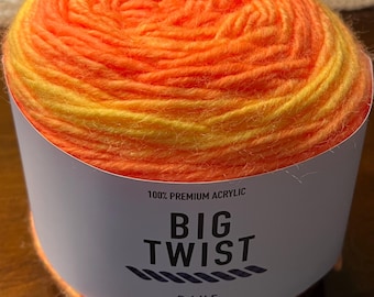 Puede incluir: Ovillo de lana Big Twist Rave naranja y amarillo vibrante. La etiqueta dice "100% Premium Acrylic" e incluye el texto "BIG TWIST RAVE". El ovillo de lana es de 205 m / 150 g.