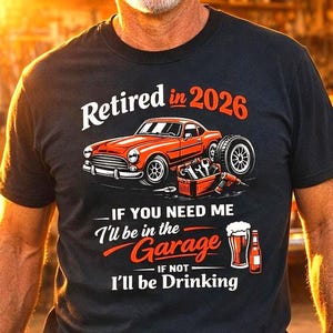 Könnte beinhalten: Schwarzes T-Shirt mit dem Text "Retired in 2026" und einer Grafik eines roten Autos, Werkzeugen und einem Bier. Das Shirt sagt auch "If you need me I'll be in the Garage, if not I'll be Drinking."