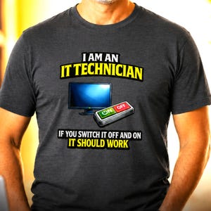 Op de afbeelding: Een antracietgrijs T-shirt met korte mouwen en een afbeelding van een computermonitor en een aan-uitknop. De tekst luidt: I AM AN IT TECHNICIAN IF YOU SWITCH IT OFF AND ON IT SHOULD WORK. De schakelaar heeft een groene ON-knop en een rode OFF-knop.