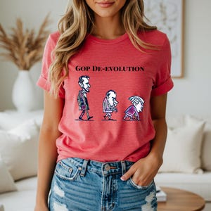 May include: Red t-shirt with the text "GOP DE-EVOLUTION" above a cartoon illustration of three figures in various stages of decline. The figures are in black and white, with the first figure standing upright, the second hunched over, and the third crawling.