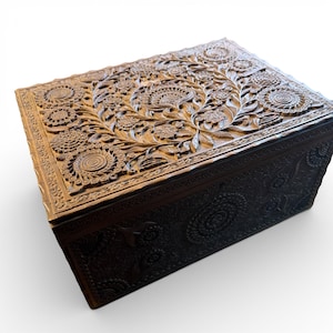 Może przedstawiać: Ciemnobrązowe drewniane pudełko z misternymi rzeźbami kwiatowymi na pokrywie i bokach. Pudełko ma prostokątny kształt i pokrywę na zawiasach. Rzeźby przedstawiają szczegółowe wzory kwiatów i liści, tworząc dekoracyjny i ozdobny design.