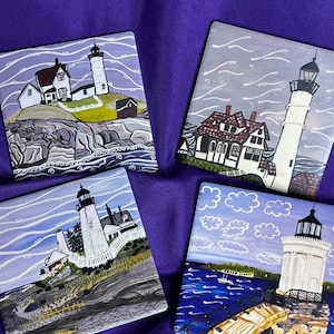 May include: Four square ceramic coasters with lighthouse paintings. Each coaster features a different coastal scene with a white lighthouse, buildings, and ocean waves. The coasters are set against a purple background.