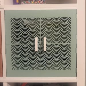 Könnte beinhalten: Hellgrüne Schranktür mit einem Wellenmuster. Der Schrank hat zwei Türen mit weißen Griffen. Die Türen sind in einem weißen Schrankrahmen eingesetzt. Das Wellenmuster ist ein sich wiederholendes Design aus Halbkreisen.