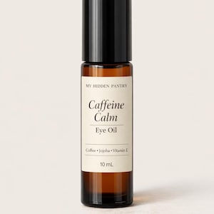Op de afbeelding: Een kleine, bruine glazen fles Caffeine Calm Eye Oil met een zwarte dop. Het etiket leest "My Hidden Pantry" en vermeldt ingrediënten: Koffie, Jojoba en Vitamine E. De fles bevat 10 ml product.