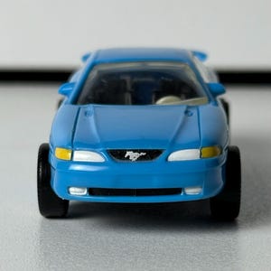 May include: A set of three ceramic mugs with a speckled, cream-colored glaze. Each mug features a different hand-painted design: a blue and green leaf, a yellow flower, and a red berry. The mugs have a capacity of approximately 12 ounces.