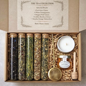 May include: A tea gift set in a cardboard box. The set includes six glass tubes of tea, a small white candle, a jar of honey, a tea infuser, and a honey dipper. The text on the box reads "THE TEA COLLECTION".