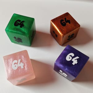 May include: Four six-sided dice in green, copper, light pink, and purple. Each die features a pearlescent finish and black or white printed numbers, including the number 64 prominently displayed on the top face of each individual cube.