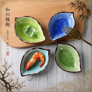 May include: Four leaf-shaped ceramic dishes in shades of green and blue, with a brown rim. One dish holds a shrimp, another ice, and the others are empty. A gold fork rests on the side. The dishes are on a wooden surface.