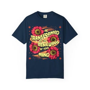 Peut inclure: T-shirt bleu marine avec un motif floral et le texte "BE TRANSFORMED BY THE RENEWING OF YOUR MIND" en jaune. Le motif comprend quatre fleurs rouges avec des centres jaunes et des étoiles oranges.