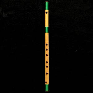 Op de afbeelding: Een cilindrische bamboe fluit met een natuurlijke lichtbruine houten afwerking, voorzien van zes vingergaten en één blaasgat. Het instrument is geaccentueerd met drie opvallende banden van felgroene draad rond de boven-, midden- en onderkant.