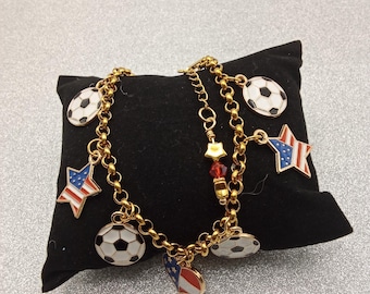 Pulseira de corrente dourada com pingentes patrióticos em esmalte, representando a seleção de futebol dos EUA.