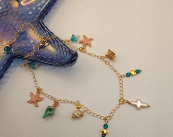 Pulseira de tornozelo dourada com pingentes coloridos de esmalte e conchas, perfeita para praia.