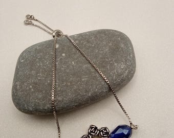 Pulsera ajustable de cadena plateada con perla central y cuentas de cristal azul en forma de lágrima.