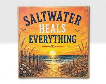 May include: A square wooden sign featuring a sunset beach scene with a wooden fence, tall grasses, and flowers. The text "SALTWATER HEALS EVERYTHING" is printed in dark blue and white letters across the center of the orange and yellow sky.