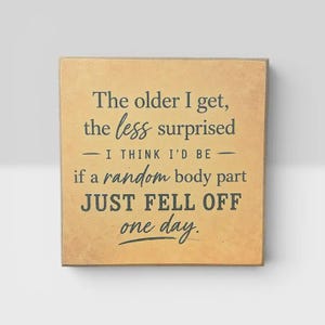 May include: A square wooden sign with a light tan, textured background and dark gray text that reads: The older I get, the less surprised I THINK I'D BE if a random body part JUST FELL OFF one day. The sign has a simple, flat, square design.