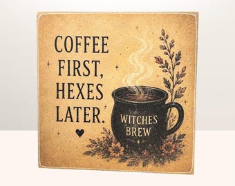 May include: A square wooden sign with a tan background featuring the black text COFFEE FIRST, HEXES LATER. A black mug labeled WITCHES BREW sits in the center with steam rising, surrounded by botanical illustrations and a small black heart.