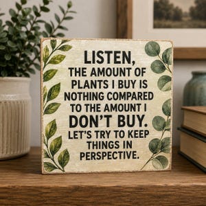 Może przedstawiać: Kwadratowy drewniany znak z postarzanym kremowym tłem i czarnym tekstem: LISTEN, THE AMOUNT OF PLANTS I BUY IS NOTHING COMPARED TO THE AMOUNT I DON'T BUY. LET'S TRY TO KEEP THINGS IN PERSPECTIVE. Ilustracje zielonych liści zdobią boki znaku.