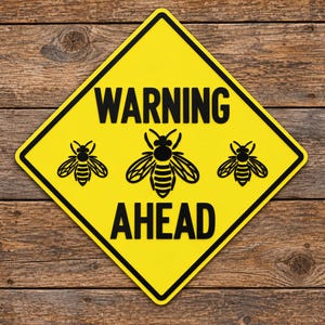 May include: A diamond-shaped yellow warning sign with a black border. The text WARNING AHEAD is printed in bold black capital letters. Between the two lines of text, there are three black graphic illustrations of bees arranged horizontally.