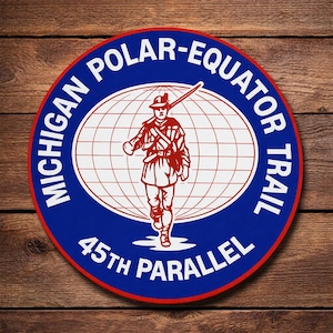 May include: A circular patch with a blue border and a red outline. The patch features the text "MICHIGAN POLAR-EQUATOR TRAIL" and "45TH PARALLEL" in white. A red illustration of a person with a rifle is in the center, set against a white globe.
